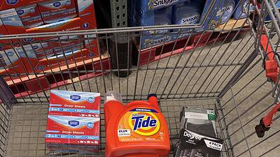 Shopping cart filled with laundry and cleaning supplies at wholesale store.