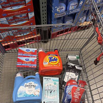 Shopping cart filled with laundry and cleaning supplies at wholesale store.
